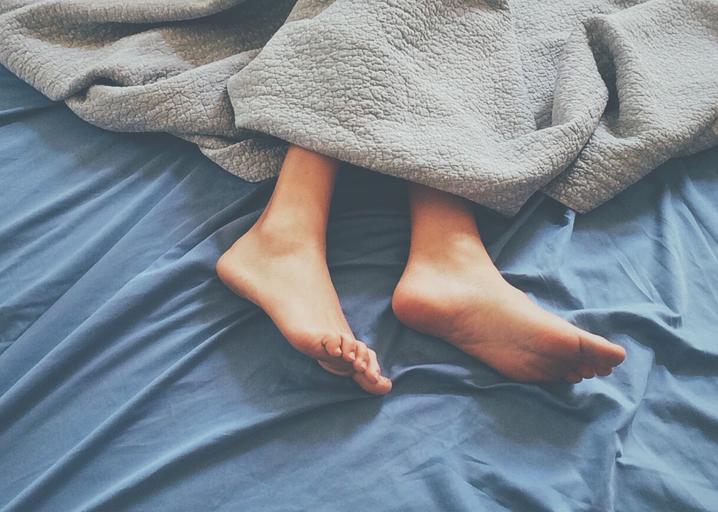 Ľudské bosé nohy zakryté paplónom na posteli s modrou plachtou.jpg
